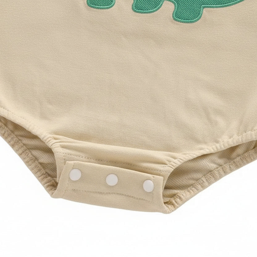 Close-up showing the three bottom snap closures for easy diaper changes on the beige long-sleeve baby bodysuit.