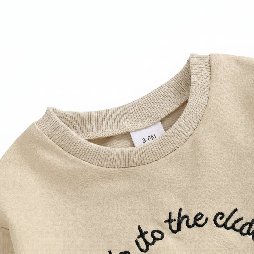 Close-up detail of the ribbed crew neckline on the beige long-sleeve baby golf romper.