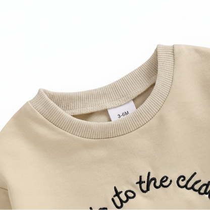 Close-up detail of the ribbed crew neckline on the beige long-sleeve baby golf romper.