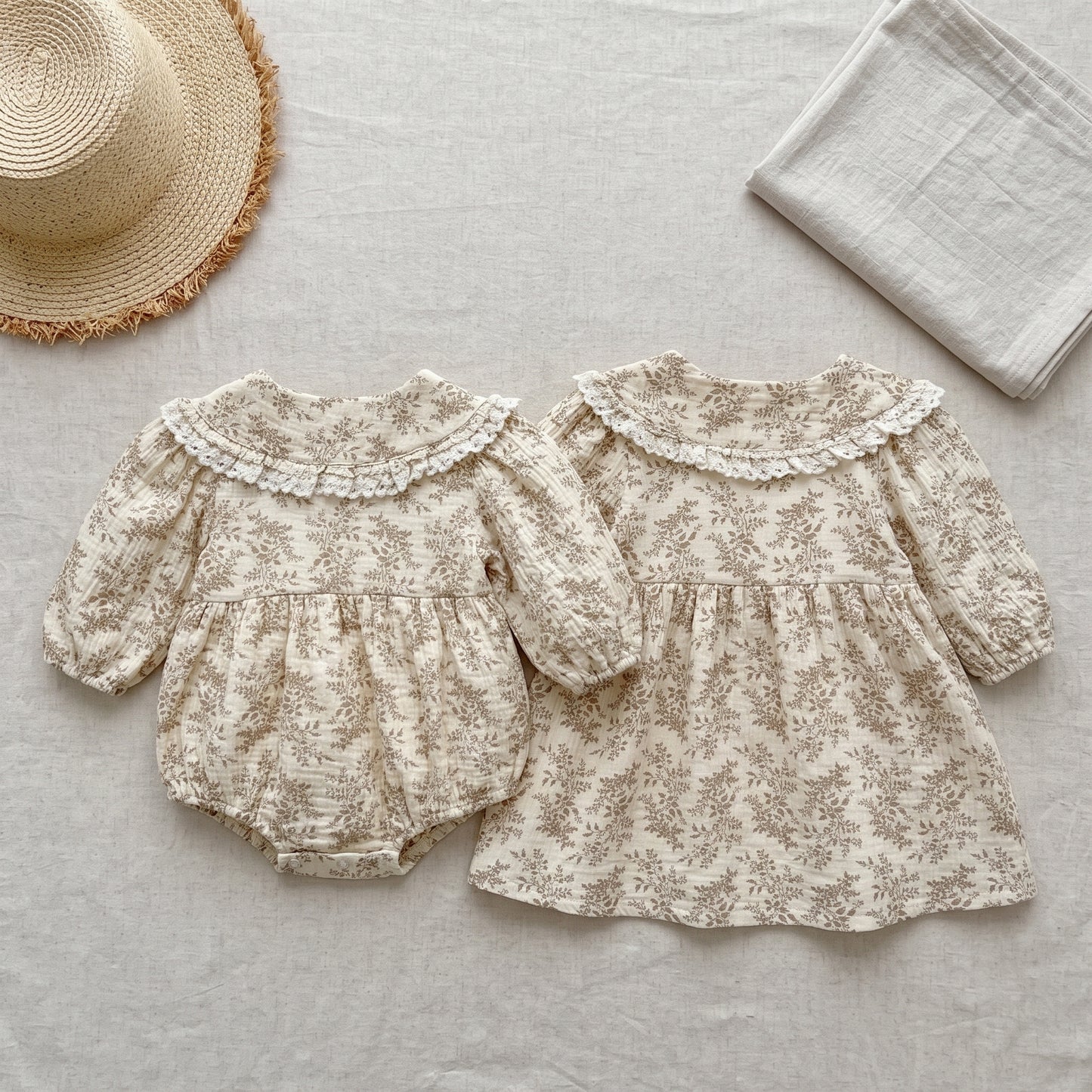 Matching baby girl floral bubble romper and toddler long sleeve dress displayed flat with a straw hat and blanket.
