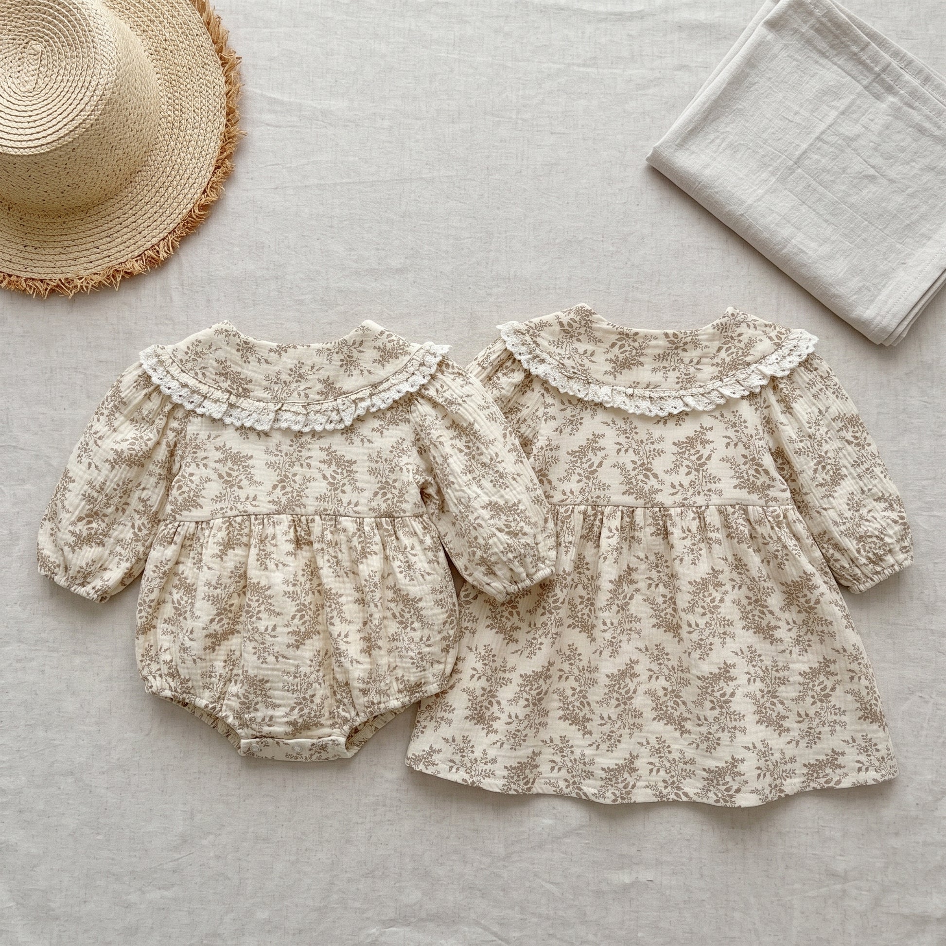 Matching baby girl floral bubble romper and toddler long sleeve dress displayed flat with a straw hat and blanket.