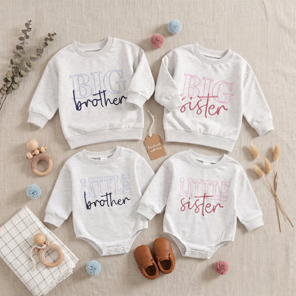 Styled flat lay of a matching sibling clothing collection featuring grey Big Brother and Big Sister sweatshirts alongside Little Brother and Little Sister bubble rompers, arranged with neutral baby accessories.