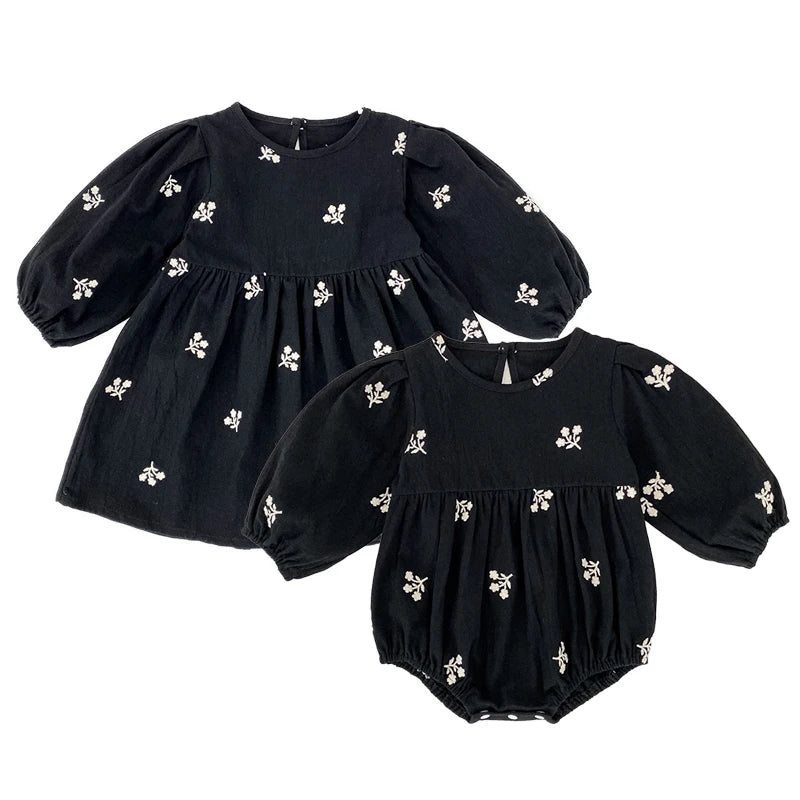 Sister matching set featuring a toddler girls black floral dress and coordinating baby girls black floral romper on a white background.