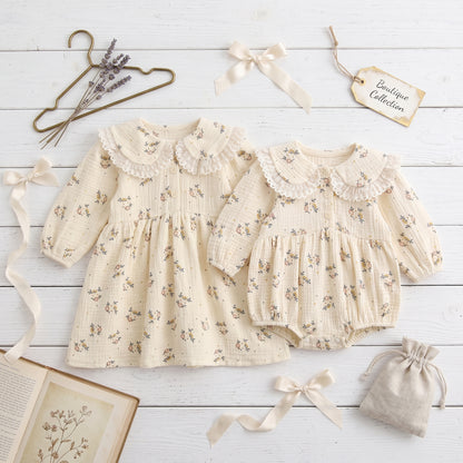 Flat lay of matching sister floral outfits including long sleeve girls dress and baby bubble romper on wood background.