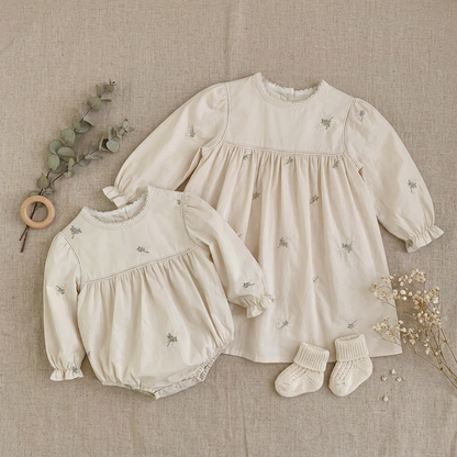 Flat lay photo of matching sister outfit set featuring long sleeve baby bubble romper and toddler dress with baby socks