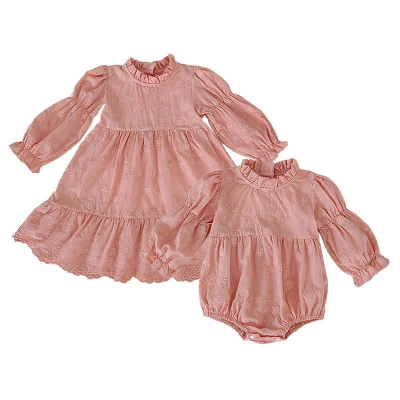 Flat lay of coordinating pink floral embroidered sister outfits, showcasing the tiered dress alongside the matching baby bubble romper.