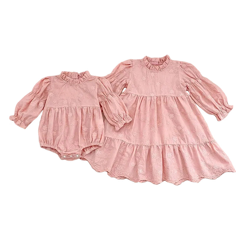 Flat lay of matching pink floral embroidered sister outfits, featuring a baby girl bubble romper next to a coordinating older sister dress.