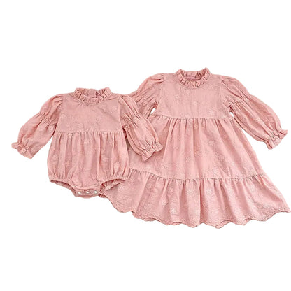 Flat lay of matching pink floral embroidered sister outfits, featuring a baby girl bubble romper next to a coordinating older sister dress.