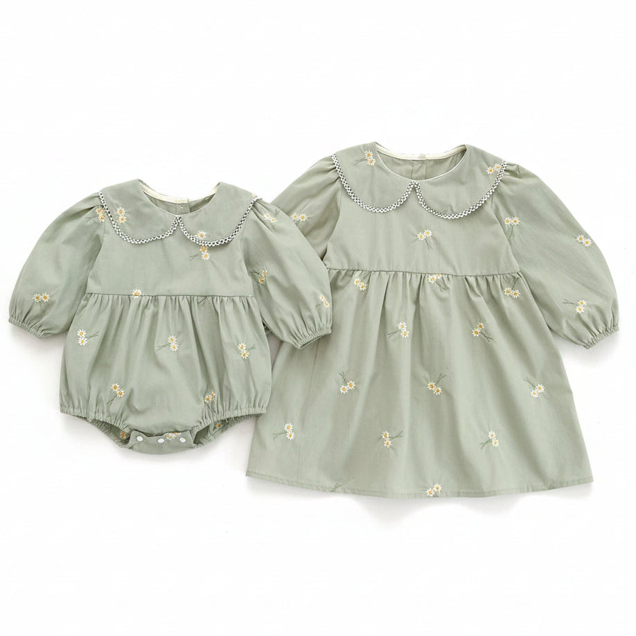 Sibling matching sister outfits featuring a coordinating sage green daisy embroidered baby romper and a matching toddler dress.