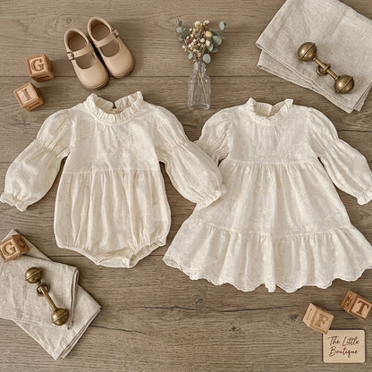 Flat lay view of matching sister set showing ivory floral embroidered baby bubble romper and girls cottagecore dress.