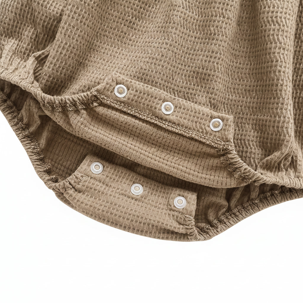 Detail view of the open bottom snap closures for easy diaper changes on the mocha waffle knit romper.