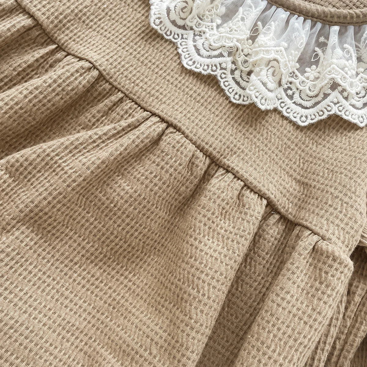 Extreme close-up of the textured cotton blend waffle knit fabric on the mocha baby girl bubble romper.