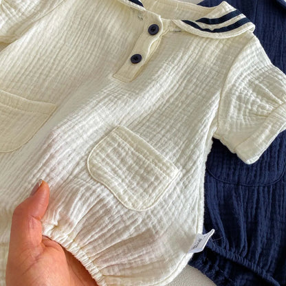 Close up of a hand holding the Sea Salt muslin romper to show the soft, breathable crinkle texture and front pocket detail.
