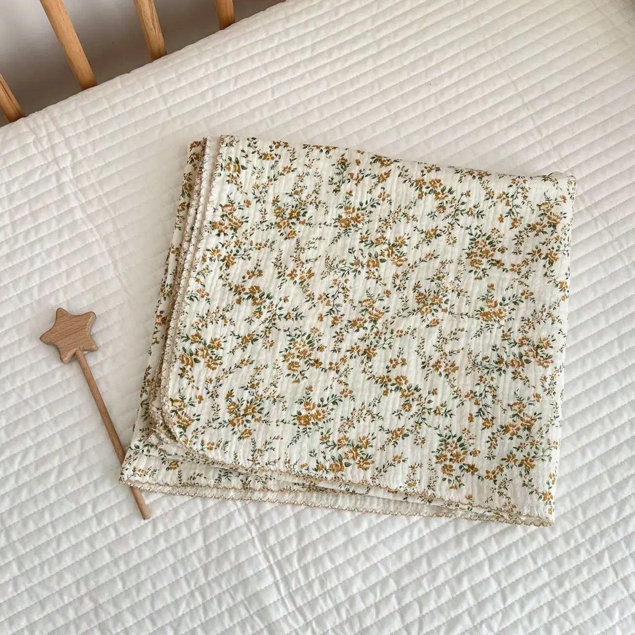Folded mustard yellow vintage floral cotton muslin baby blanket styled in a crib setting.