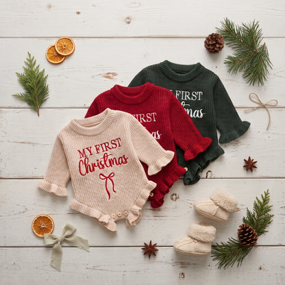 Flat lay of beige, red, and dark green baby girl My First Christmas knit sweater rompers with holiday decorations.