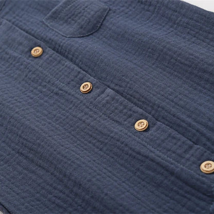 Detail shot of the functional rustic wooden-style buttons on the front of the neutral baby muslin jumpsuit.