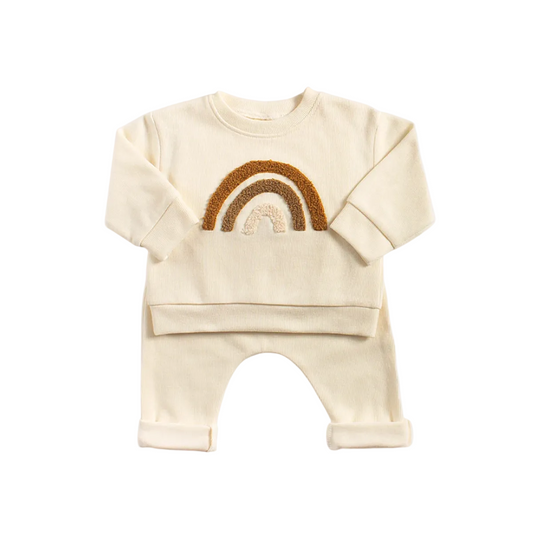 Cream baby pullover sweatshirt featuring a textured earth-tone rainbow design with matching knit leggings hanging on a wooden rack.