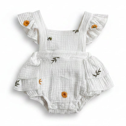 Front view of a white cotton muslin baby girl romper featuring yellow sunflower and daisy embroidery, ruffle flutter sleeves, and snap closures on a white background.