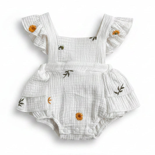 Front view of a white cotton muslin baby girl romper featuring yellow sunflower and daisy embroidery, ruffle flutter sleeves, and snap closures on a white background.