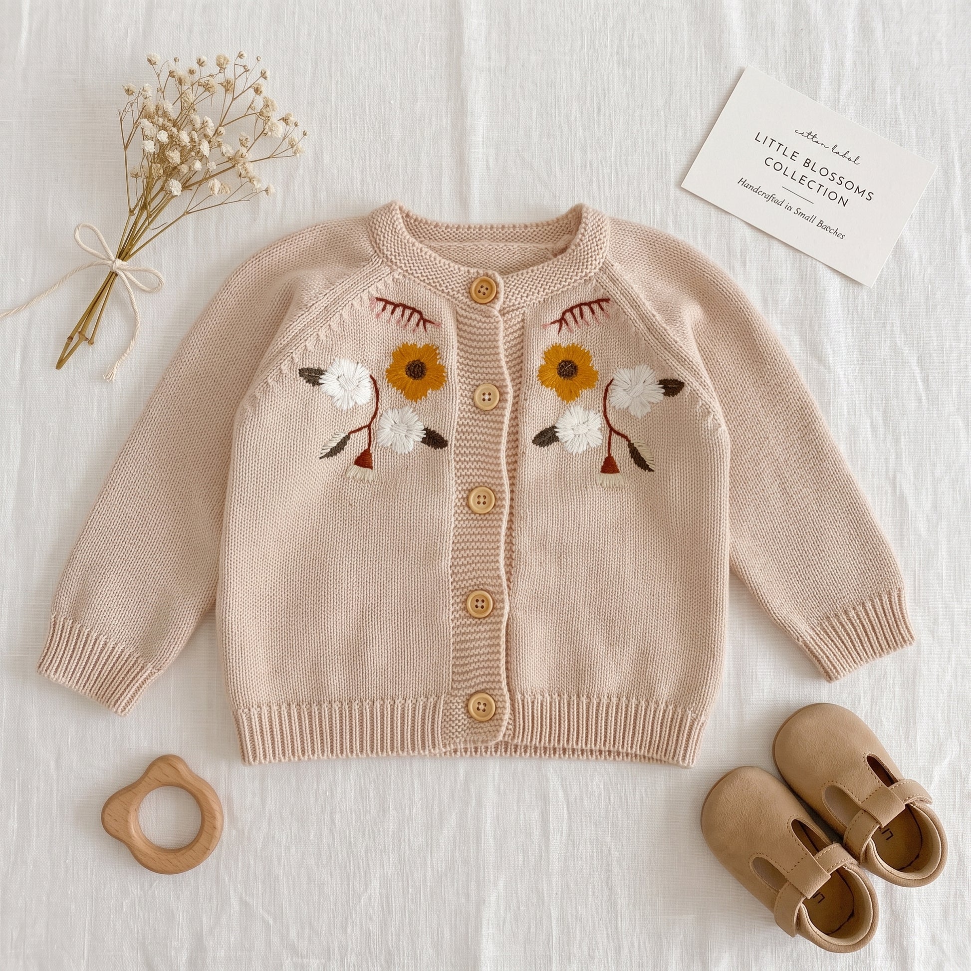Flat lay of oatmeal baby floral embroidered knit cardigan sweater styled with baby shoes