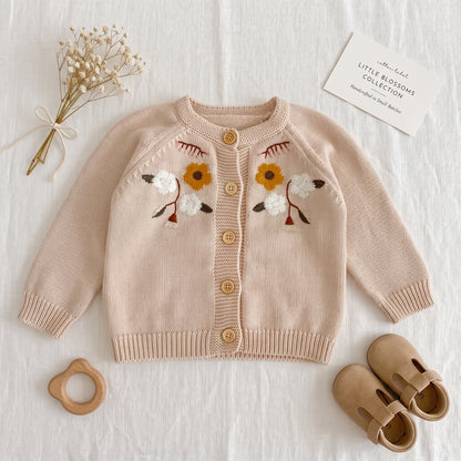 Flat lay of oatmeal baby floral embroidered knit cardigan sweater styled with baby shoes