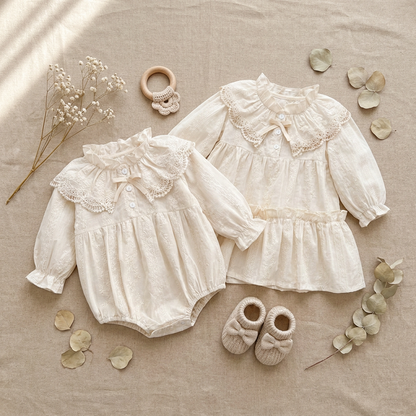 Flat lay of matching off-white lace baby bubble romper and toddler tiered dress with vintage accessories.
