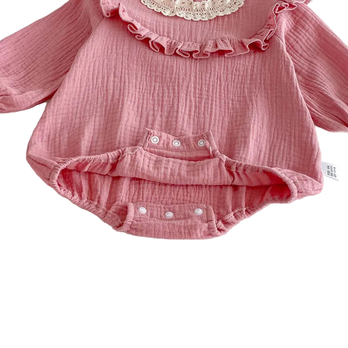Detail shot of the open bottom gusset on a pink muslin baby romper showing the interior finishing and open snap buttons.