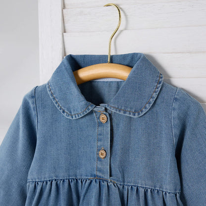 Close-up detail of the Peter Pan collar and wooden-style front buttons on a girls' blue denim jumpsuit on a hanger.