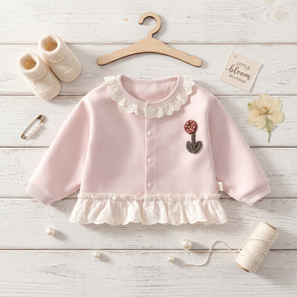 Flat lay presentation of a pink baby girl floral lace cardigan sweater styled with a wooden hanger and knit booties.