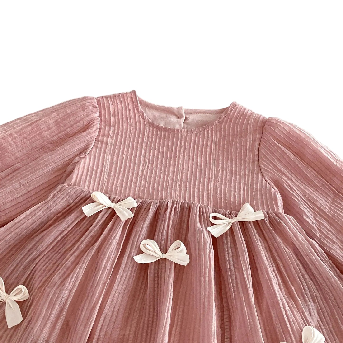 Detailed view of the chest and waistline of the dusty pink baby dress highlighting the textured pleats and white ribbon bows.