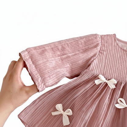 Close-up of a hand holding the sleeve of the dusty pink baby dress to highlight the stretchy elastic ruffle cuff detail.