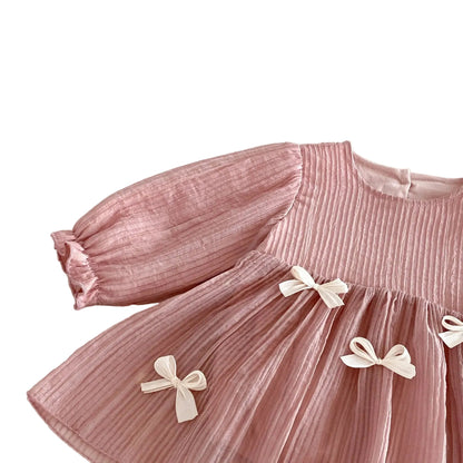 Side angle view of the dusty pink long sleeve baby romper dress showing the drape, volume, and texture of the pleated fabric.