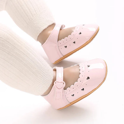 Baby girl feet wearing pink heart-cutout Mary Jane soft-sole shoes.