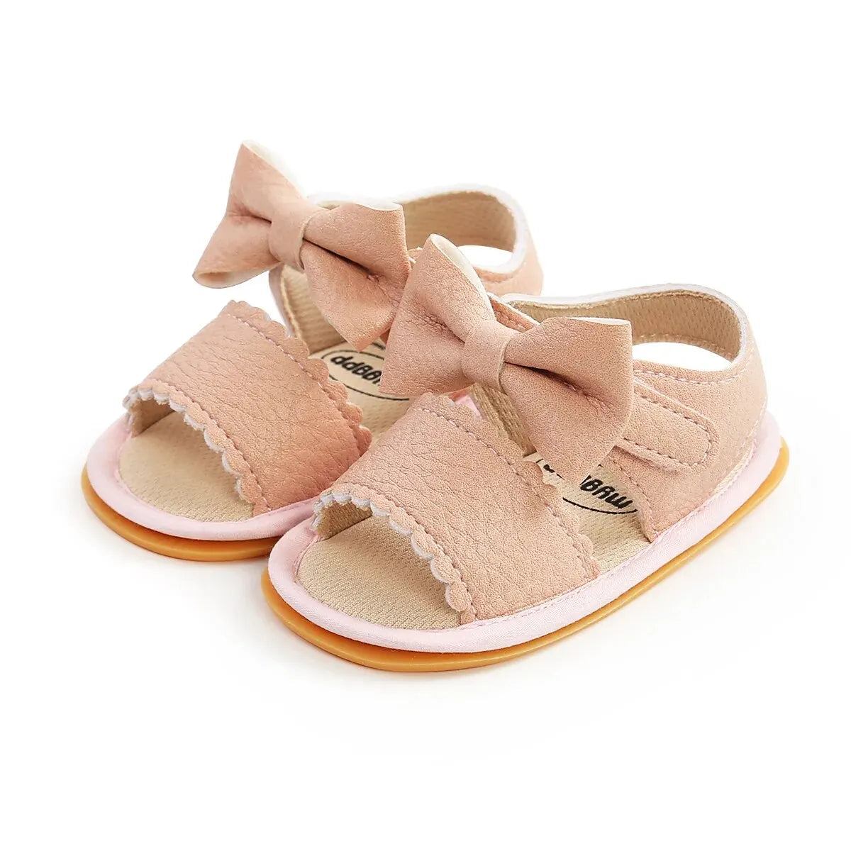 Pair of pink leather baby girl first walker sandals featuring an adjustable side strap, textured scalloped trim, and a decorative bowknot on a flat rubber sole.