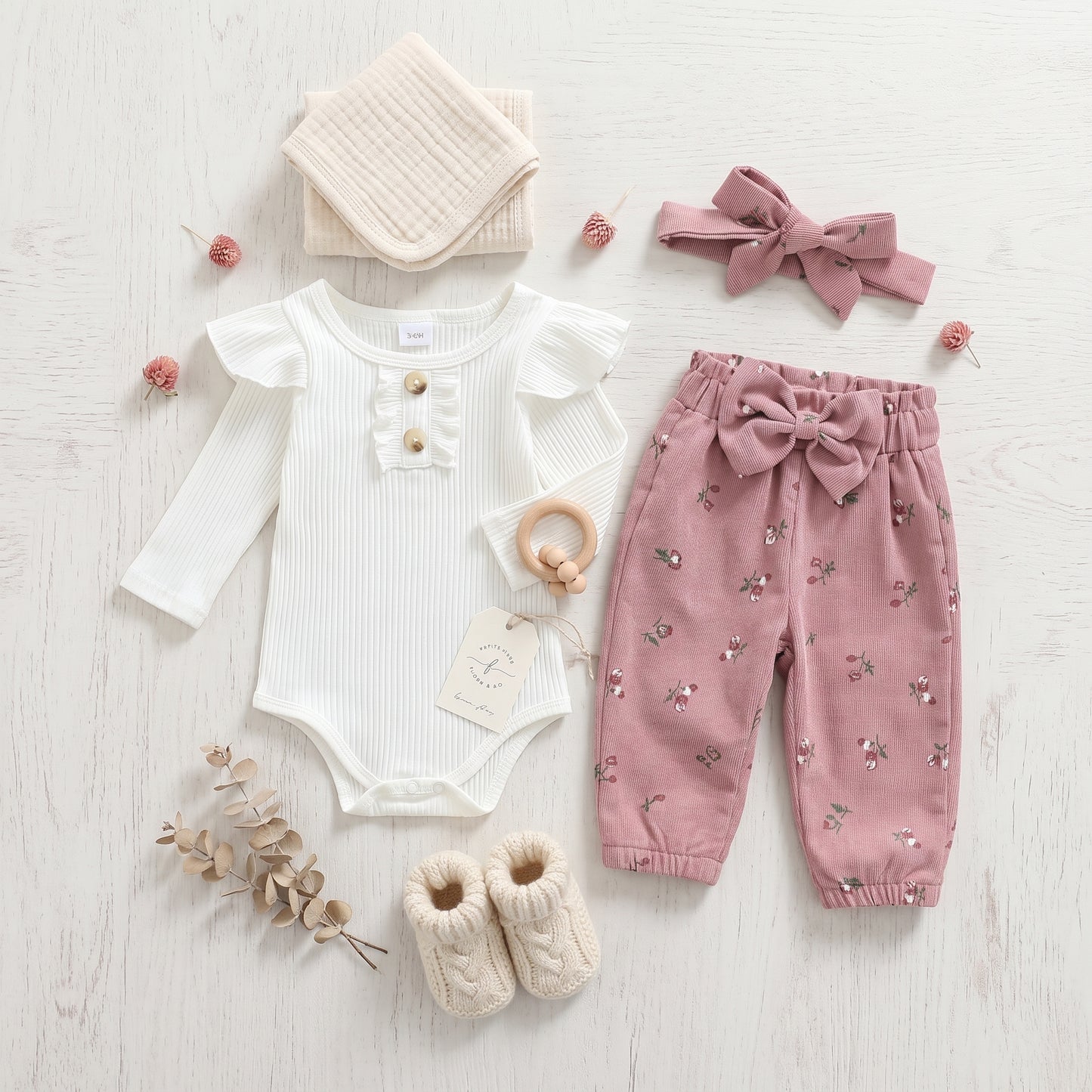 Styled flat lay of baby girl fall clothing set including a white ruffled romper, pink floral corduroy pants, headband, and baby booties.