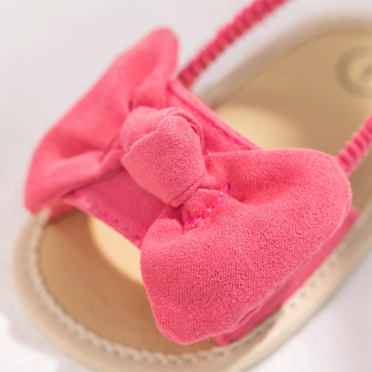 Close-up of the soft brushed fabric pink bow on a baby girl's soft sole sandal.