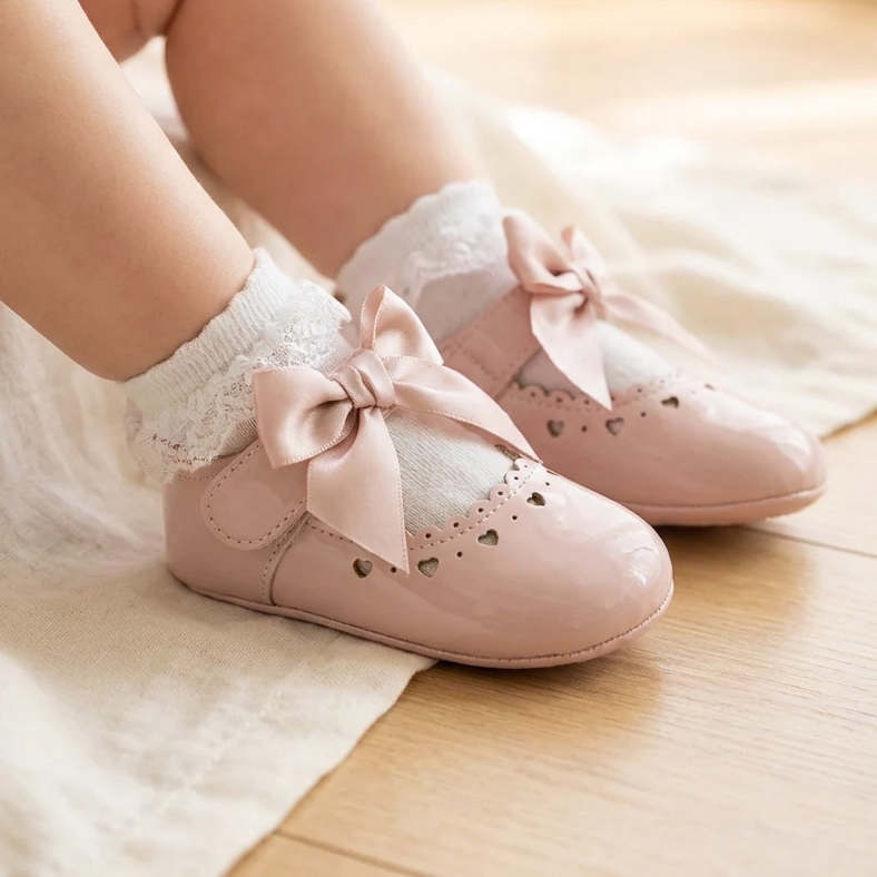 Baby sitting on a wooden floor wearing pink Mary Jane dress shoes with white lace-trimmed socks.