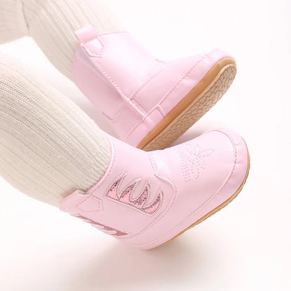 Close up of pink baby cowgirl boots on an infant's feet, showing the textured anti-slip rubber outsol