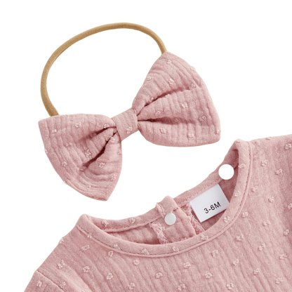 Close-up of a pink textured baby bow headband placed next to the button-up crew neckline of a matching romper.