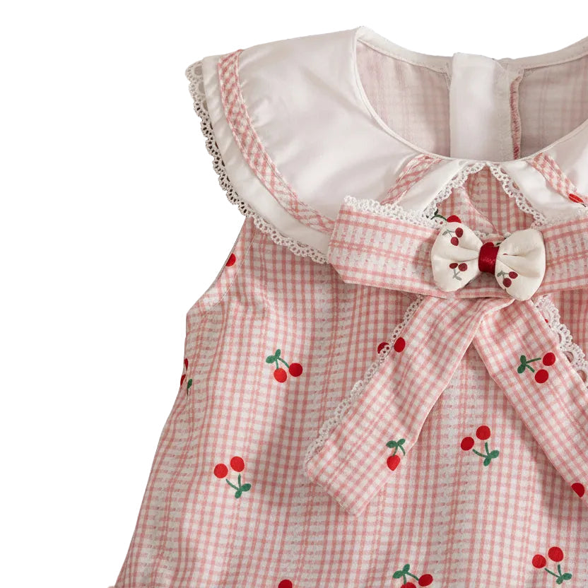 Close-up detail of the white ruffle Peter Pan collar and center bow with cherry appliqué on the pink gingham dress.