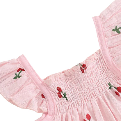 Detailed close-up of the blush pink smocked top, highlighting the elastic bodice and delicate fly sleeves with red cherry print.