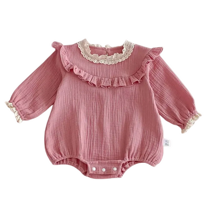 lat lay of a dusty pink long-sleeve cotton muslin baby girl romper featuring a vintage lace collar and chest ruffle on a white background.