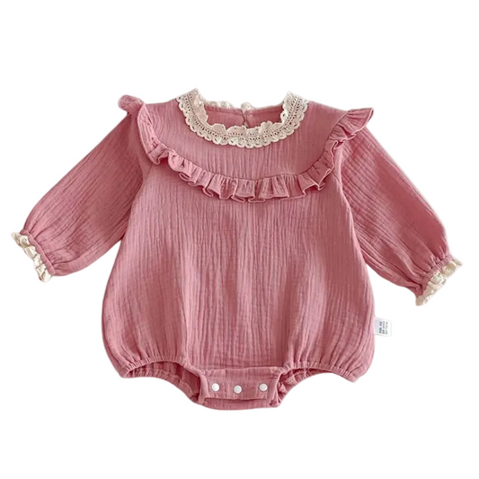 lat lay of a dusty pink long-sleeve cotton muslin baby girl romper featuring a vintage lace collar and chest ruffle on a white background.