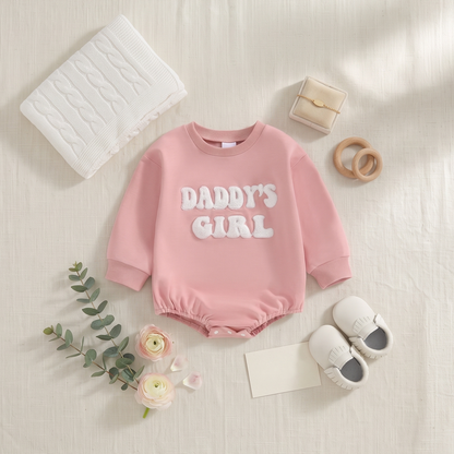 Styled flat lay of the pink "Daddy's Girl" baby sweatshirt bubble romper next to baby shoes and accessories.