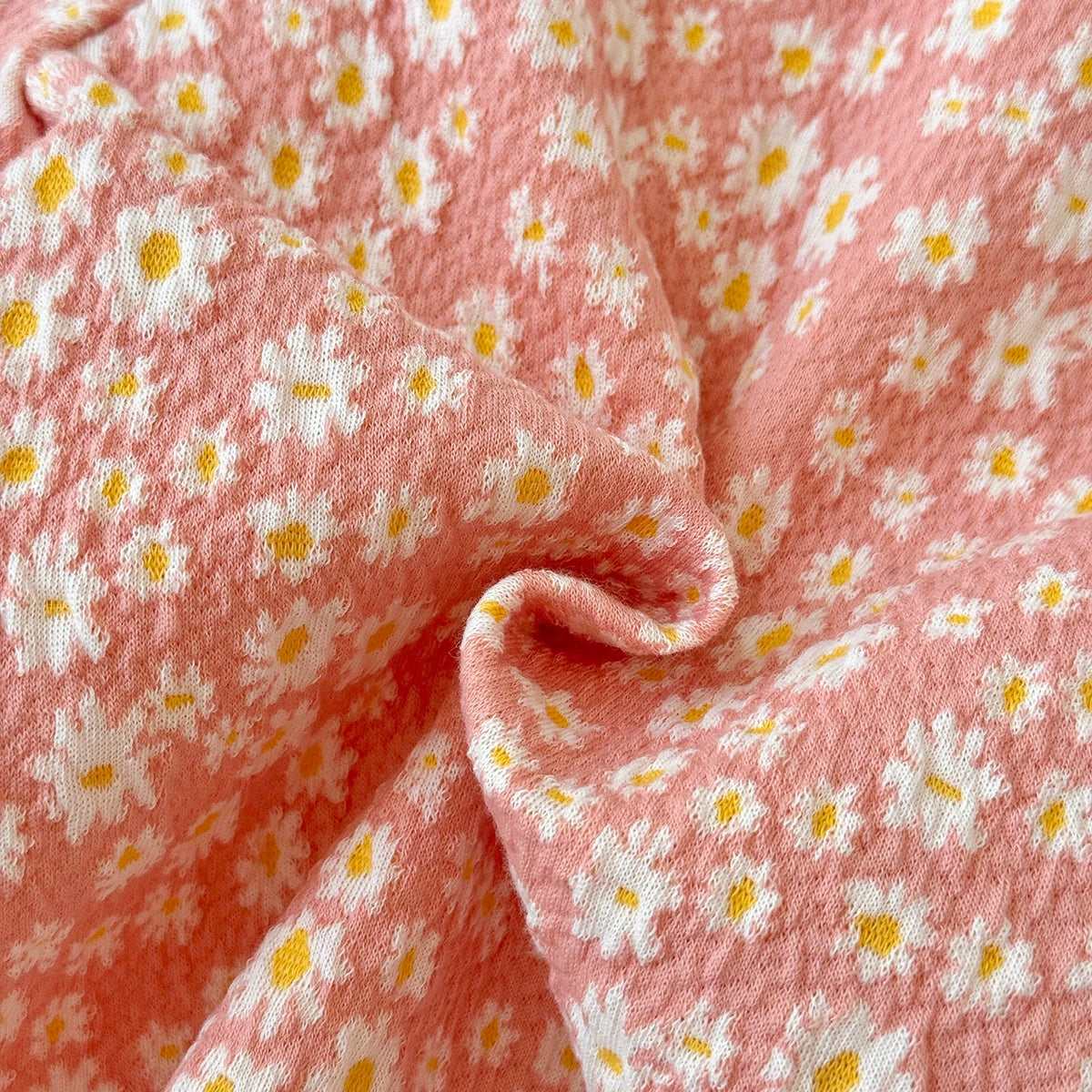 Close-up detail showing the textured pink fabric and the white and yellow daisy print of the baby romper.