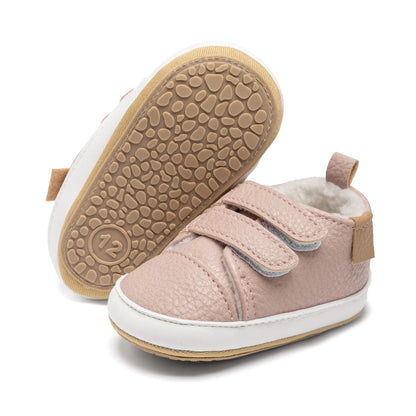One pink infant sneaker standing upright next to another showing the flexible, textured anti-slip rubber sole.