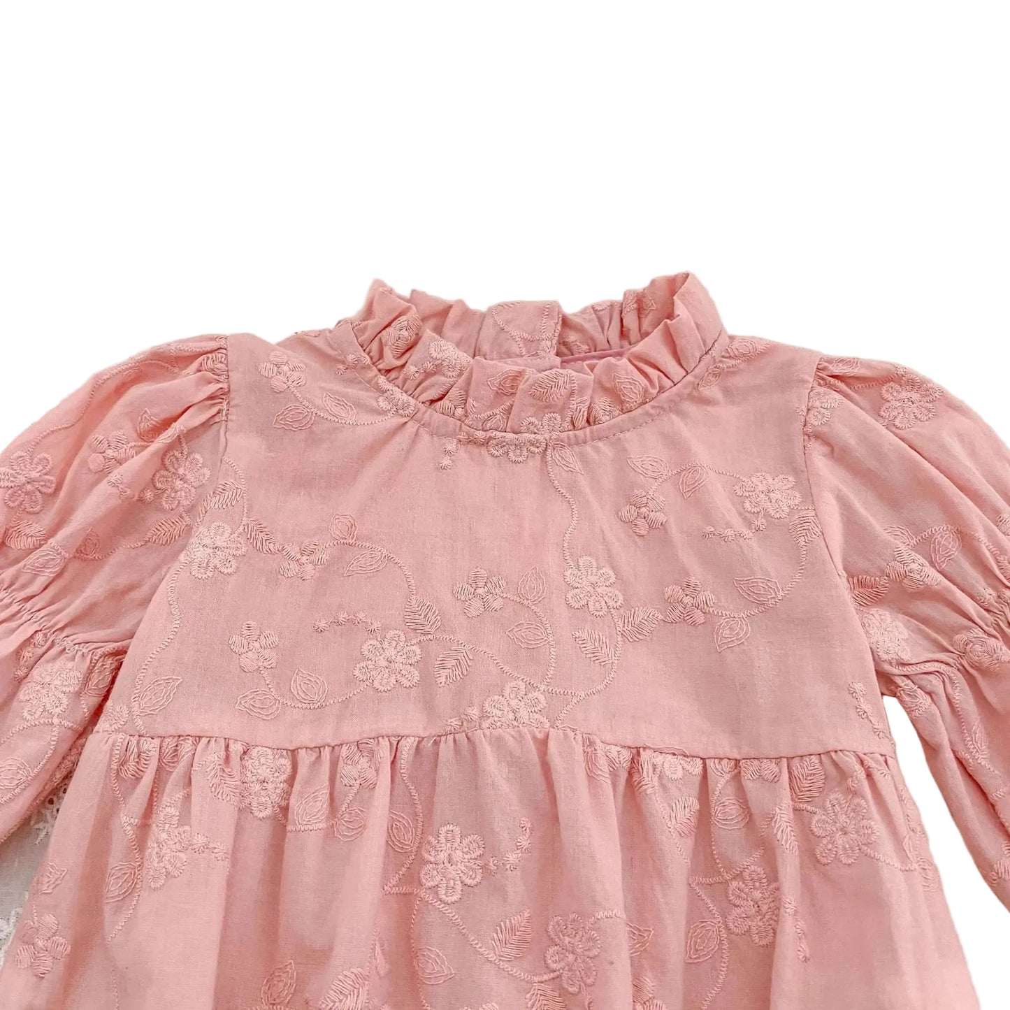 Close-up detail of the ruffle mock neckline and textured floral embroidery on a pink cotton baby romper.