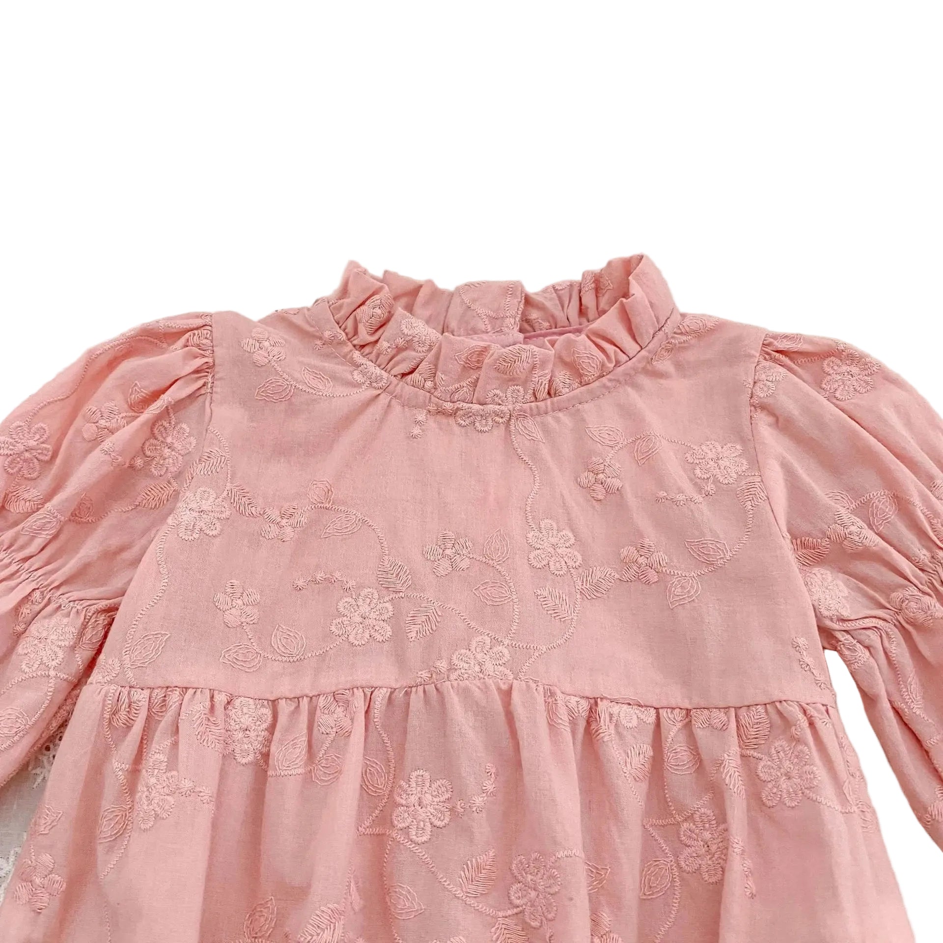 Close-up detail of the ruffle mock neckline and textured floral embroidery on a pink cotton baby romper.