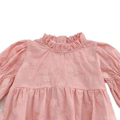 Close-up detail of the ruffle mock neckline and textured floral embroidery on a pink cotton baby romper.