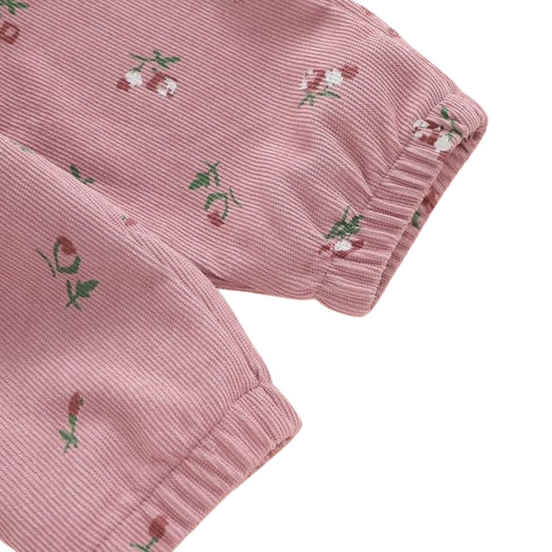 Close-up of pink floral corduroy fabric on baby girl pants showing the ribbed texture, floral print, and elastic ankle cuffs.